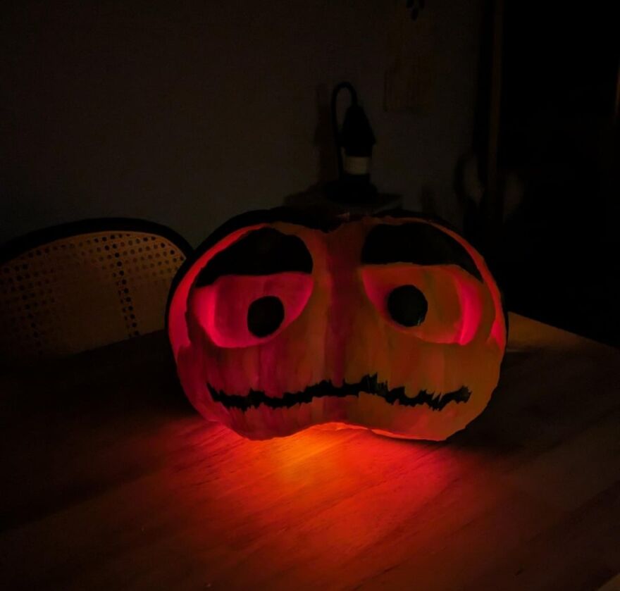 Carved pumpkin with quirky glowing eyes and mouth, showcasing a charming and spooky pumpkin carving design on a table.