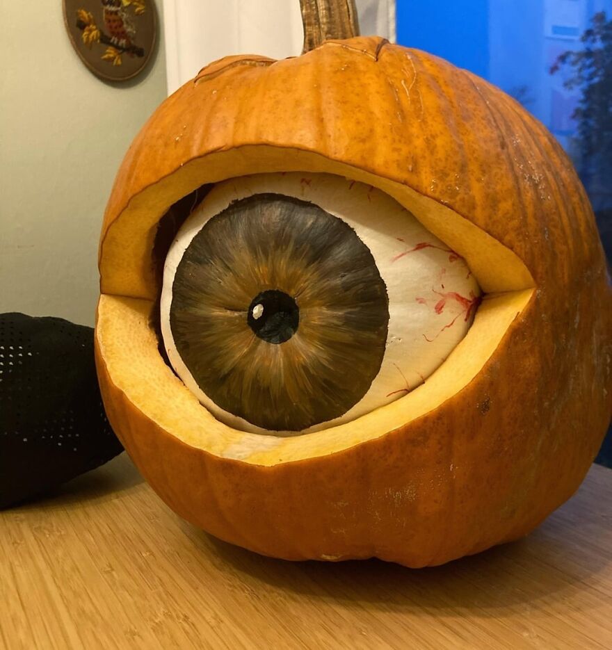 Pumpkin carving showing a spooky eye inside a hollowed pumpkin on a wooden surface with a blue background.