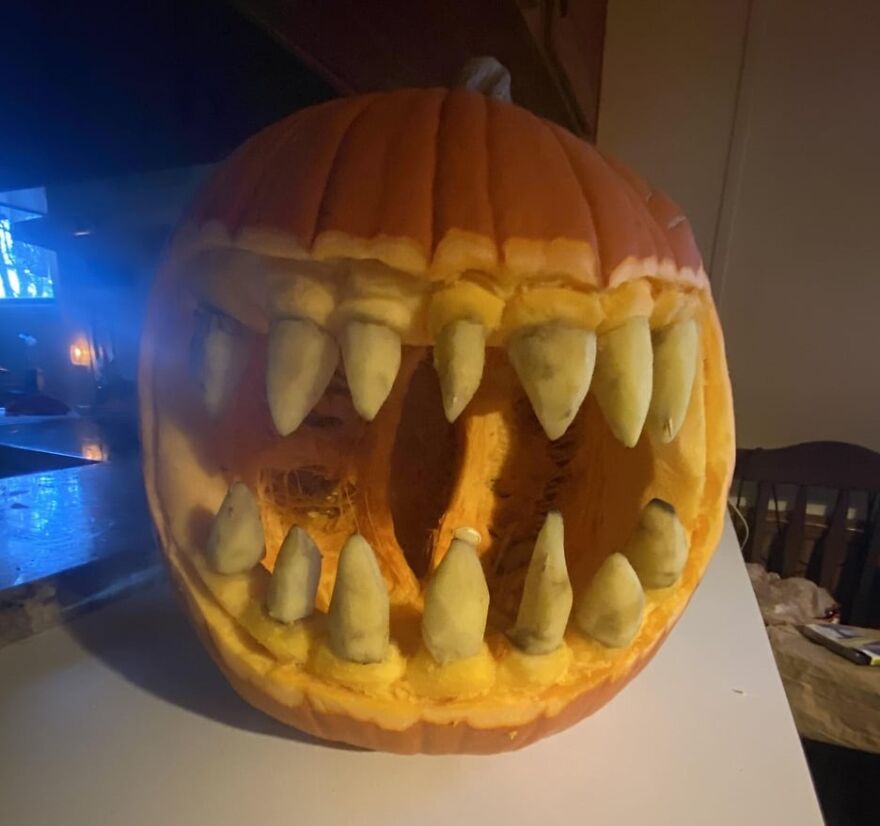 Pumpkin carving with large, jagged teeth creating a spooky and quirky Halloween decoration indoors on a table.