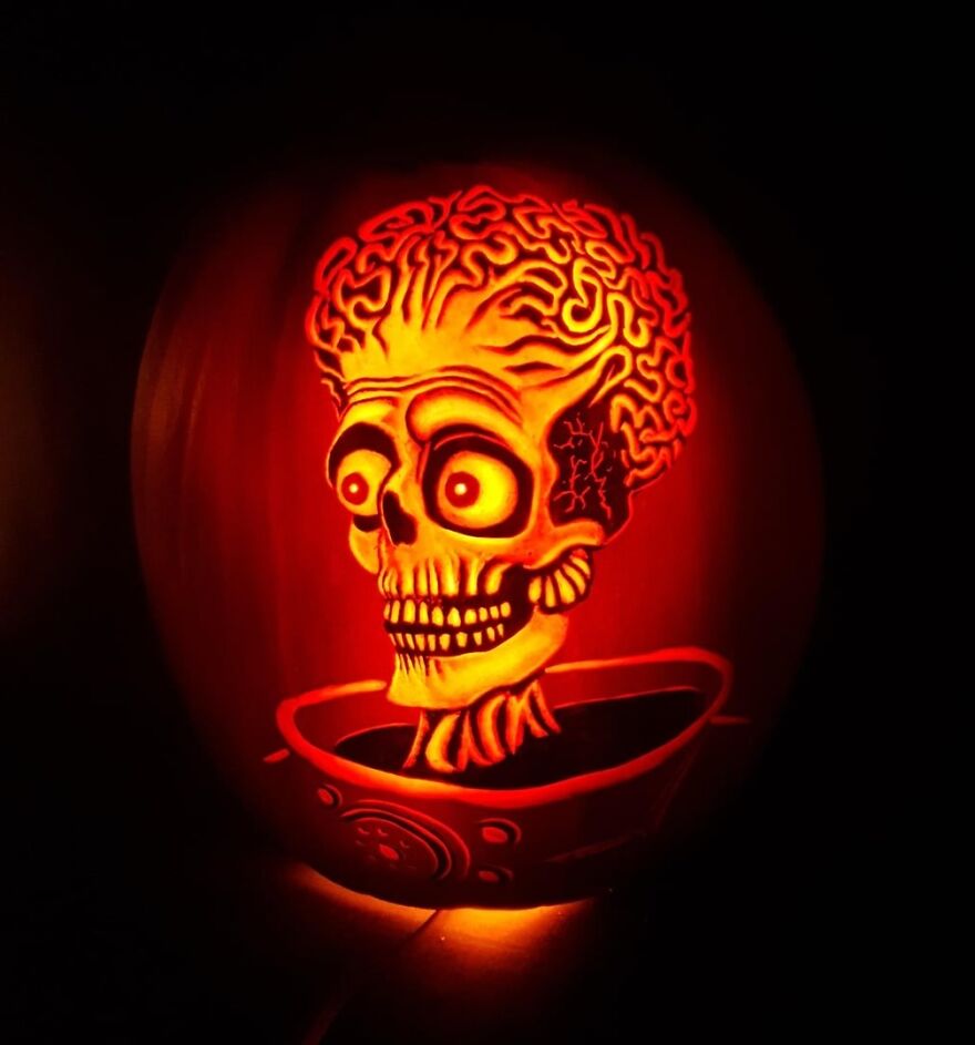 Pumpkin carving of a quirky skeleton head with exposed brain illuminated from inside in a dark setting.