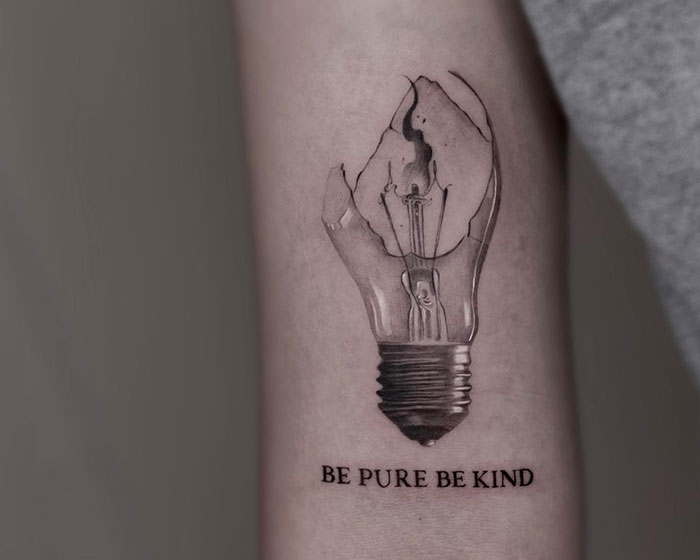 Minimalistic tattoo ideas for men featuring a broken light bulb design with intricate shading, paired with the motivational text “Be Pure Be Kind” underneath for a symbolic touch.