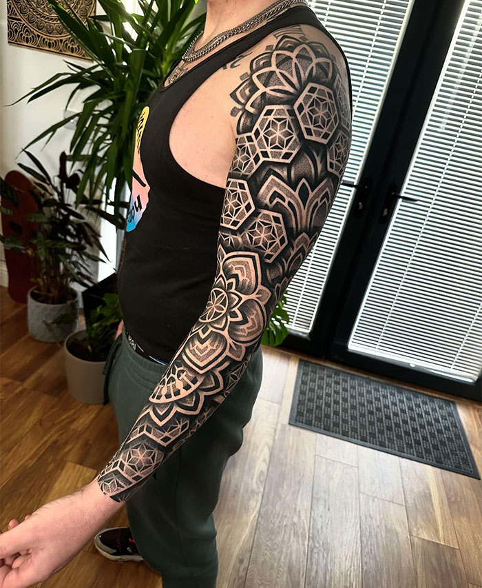 A man showcasing a full-sleeve tattoo featuring intricate geometric patterns and mandala designs, combining dark shading and detailed linework. Tattoo ideas for men focusing on symmetrical, bold blackwork and modern geometric aesthetics.