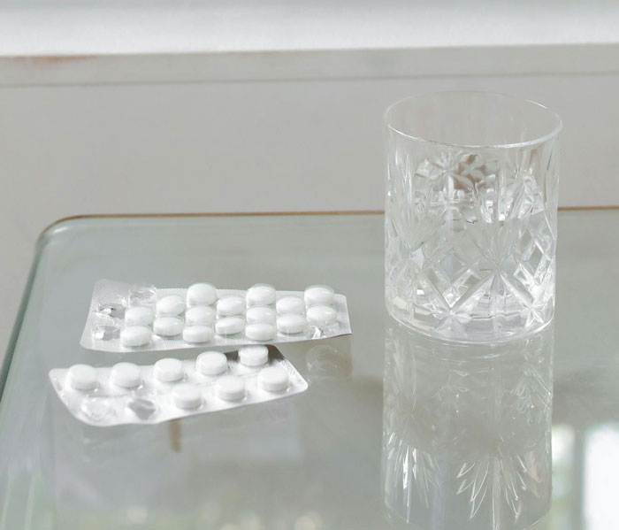 Clear glass of water next to blister packs of white pills on a reflective surface, representing stories about Kevin