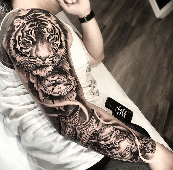  A full-sleeve tattoo featuring a realistic tiger head, a detailed compass, and intricate architectural designs. Tattoo ideas for men seeking a powerful and dynamic arm piece that symbolizes strength, direction, and a connection to heritage.