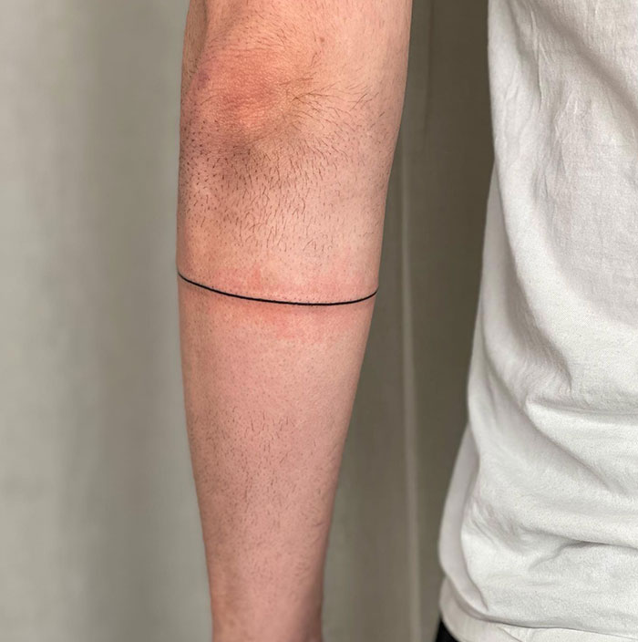  A minimalist single-line armband tattoo encircling the lower bicep, offering a clean and simple look. Tattoo ideas for men seeking subtle and understated designs.
