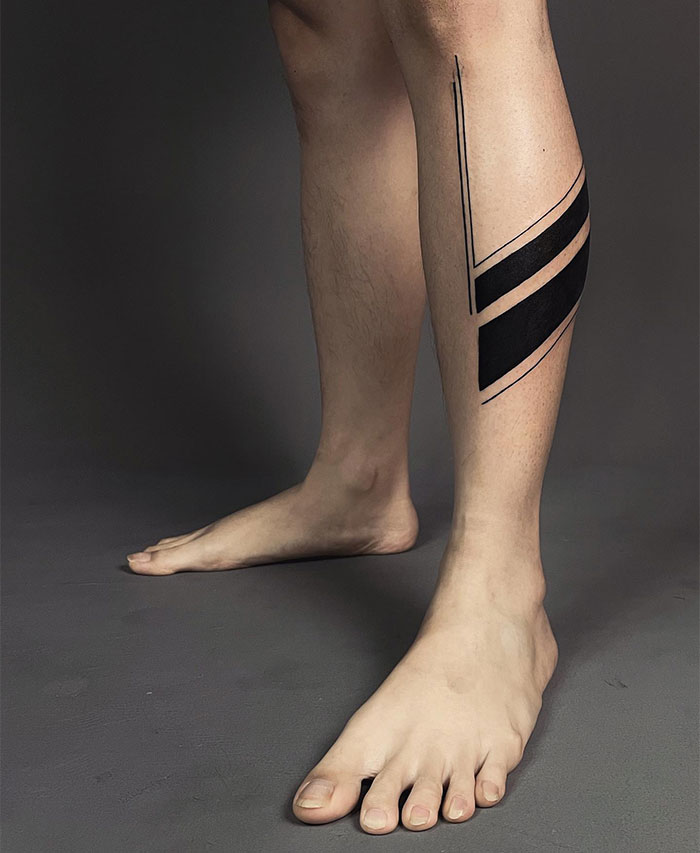 A minimalist geometric leg tattoo featuring three sharp diagonal black stripes intersected by thin lines. Tattoo ideas for men seeking sleek, modern, and bold designs.