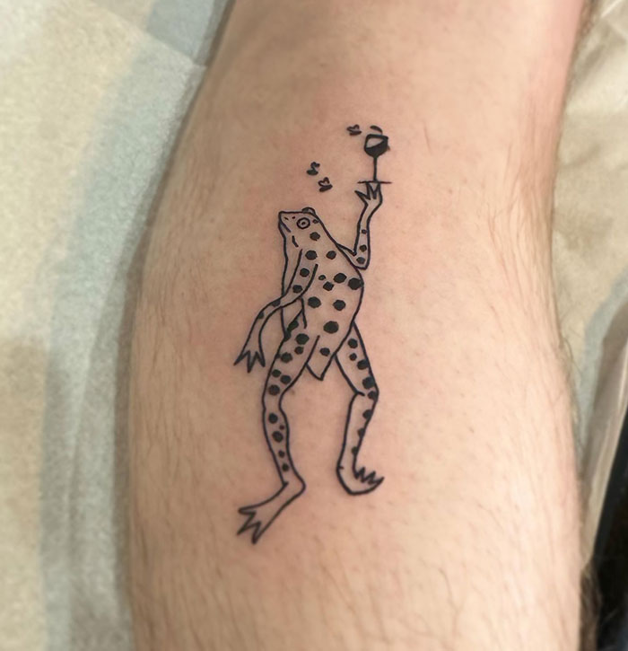 Line tattoo of a whimsical frog holding a glass, with musical notes floating around. Tattoo ideas for men looking for a playful and minimalist design.