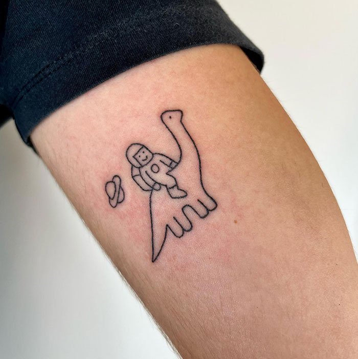Minimalist tattoo of an astronaut riding a cute dinosaur, with tiny planets floating nearby. Tattoo ideas for men seeking fun and imaginative designs.
