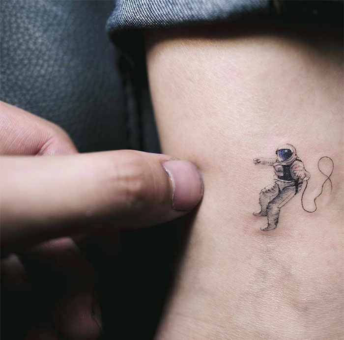 A small tattoo of a floating astronaut in a spacesuit, with a minimalist design. A subtle yet adventurous tattoo idea for men, symbolizing exploration and curiosity.