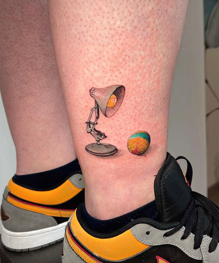 A tattoo featuring a classic desk lamp alongside a colorful ball, inspired by a famous animated studio's iconic logo. A nostalgic and creative tattoo idea for men.