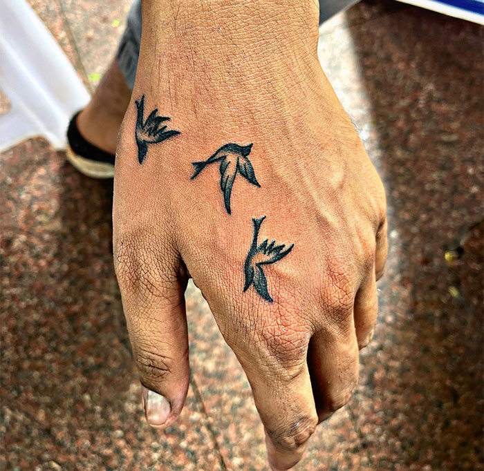  Three small black bird silhouettes tattooed on the hand, symbolizing freedom and movement. A minimalist and expressive tattoo idea for men.