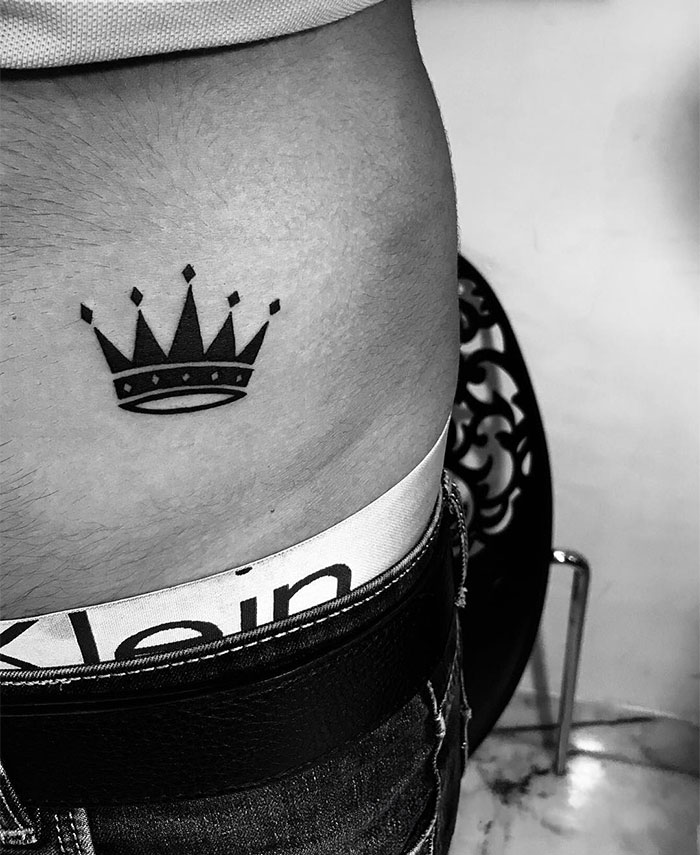 A small black crown tattoo placed on the lower side of the torso, symbolizing power, confidence, and self-worth. A sleek and classic tattoo idea for men.