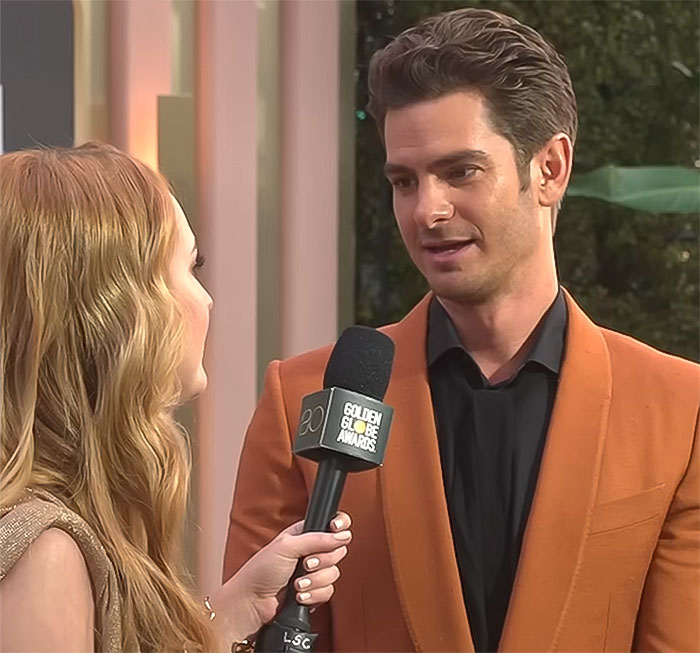 A man in an orange suit and a woman interviewing him at the Golden Globe Awards, focusing on seduction and charm.