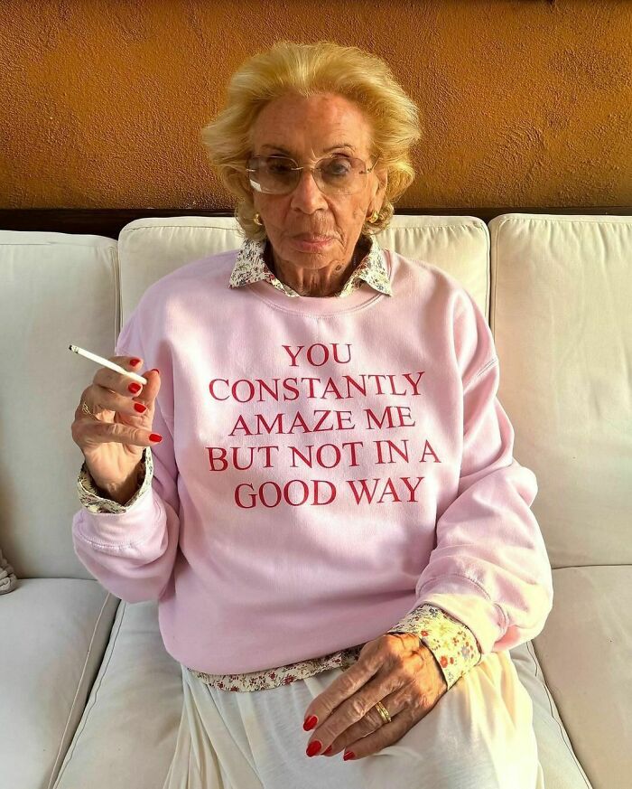 Elderly woman in a pink sweatshirt with a sarcastic quote, holding a cigarette, adding random humor to brighten your day.