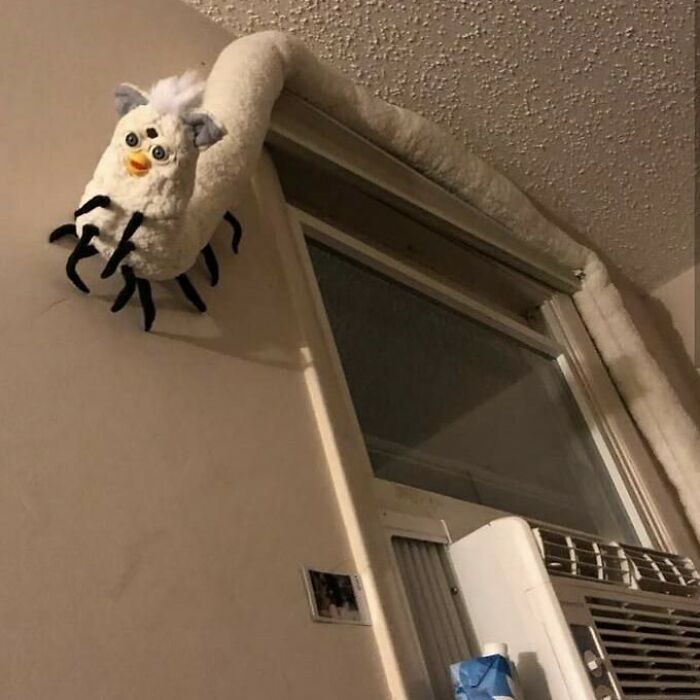 A bizarre plush decoration resembling a spider with a furby head wrapped around a window in a dark room.