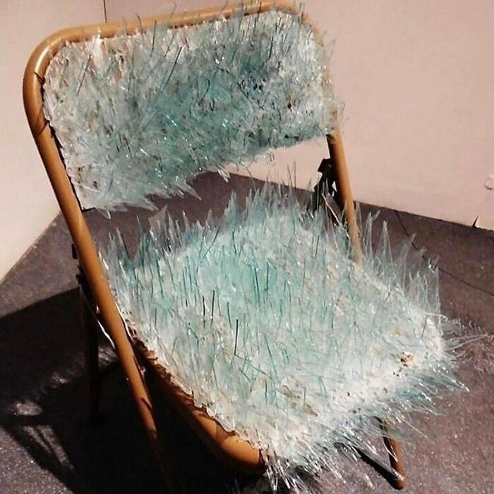 Folding chair covered in sharp broken glass shards, highlighting bizarre reality with a dark, hilarious twist in a strange scene.