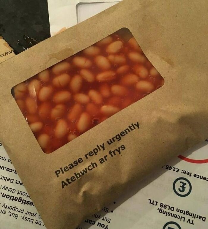 Baked beans visible through a clear window on a paper envelope labeled with a humorous, misspelled urgent message.