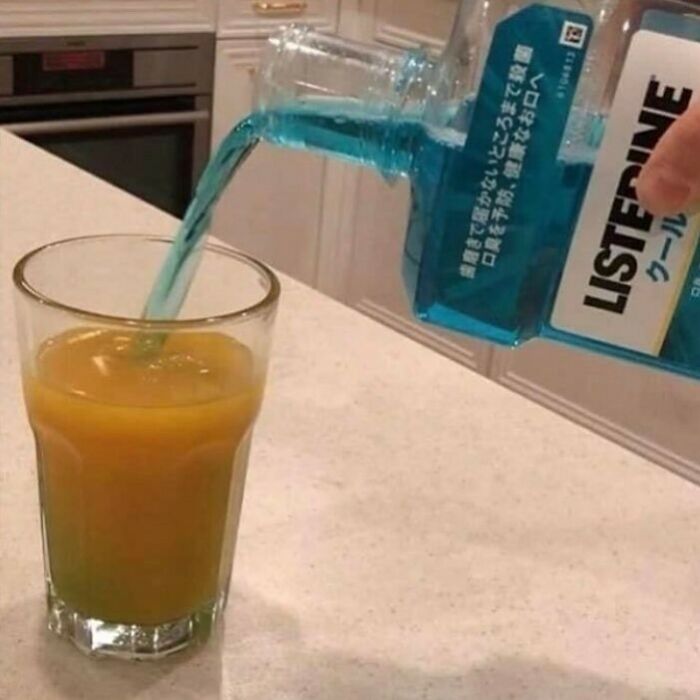 Pouring blue mouthwash into a glass of orange juice, a bizarre twist on reality captured in a strange photo.