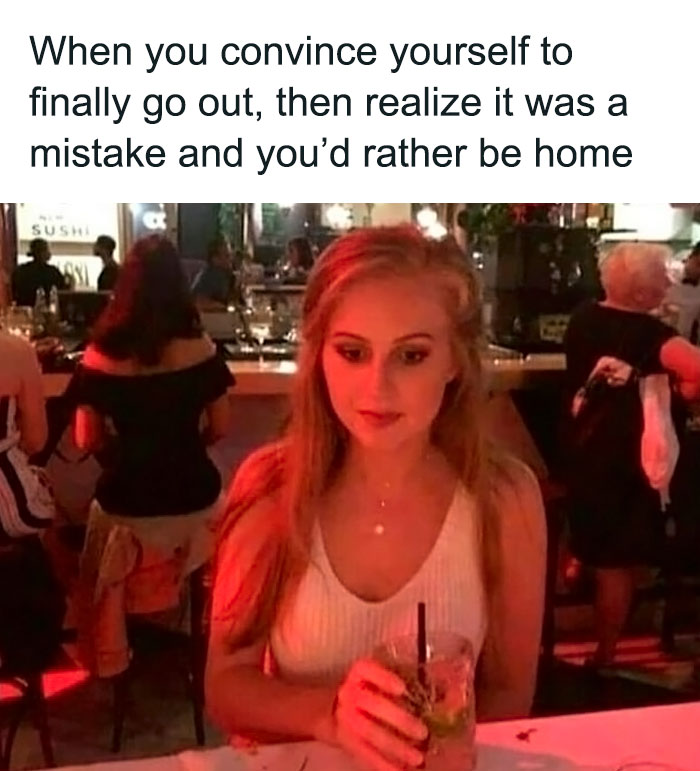 Young woman at a bar looking hesitant and holding a drink, depicting relatable introvert life meme about regretting going out.