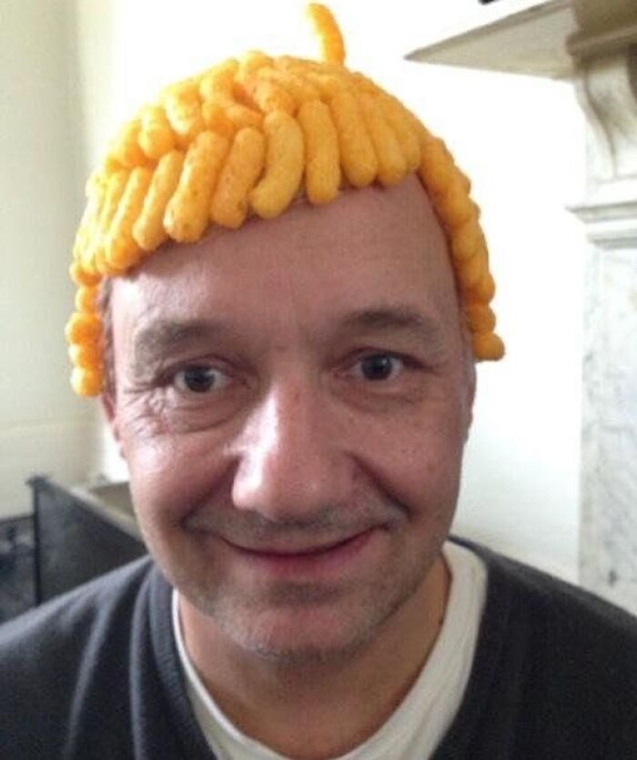 Man wearing a hat made of cheese puffs, showcasing bizarre pics with a dark, hilarious twist on reality.