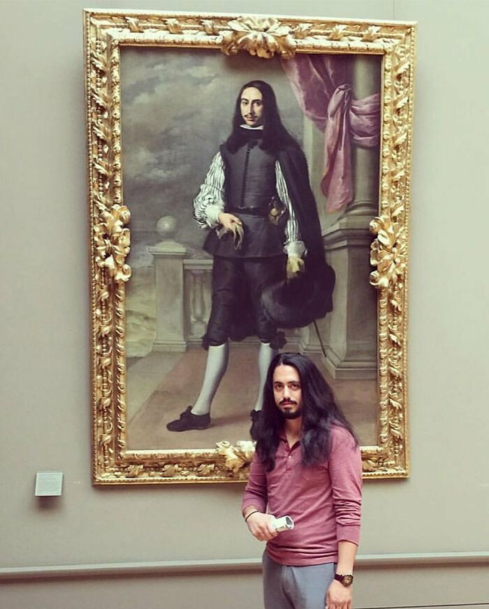 Man with long hair posing beside a historic portrait in a museum, a delightfully random photo to brighten your day.