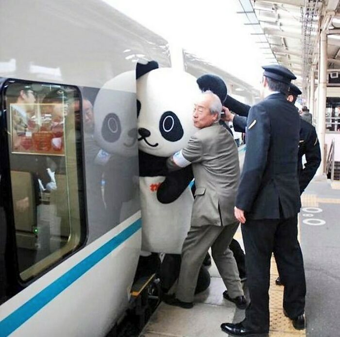 Man in suit helping person in panda costume board a train, a delightfully random photo to make your day brighter.