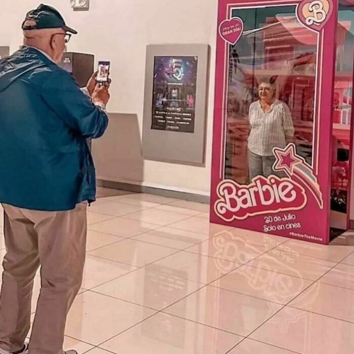 Elderly man takes photo of woman posing inside a giant Barbie box in a delightfully random photos moment.