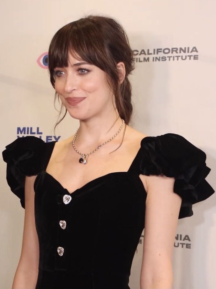 Smiling woman in a black dress at a film event; discussing actors in movie roles.