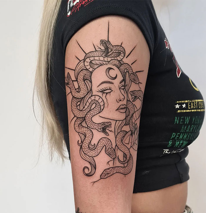 Minimalist Medusa tattoo on upper arm with snakes and crescent moon, symbolizing beauty, power, and defiance.