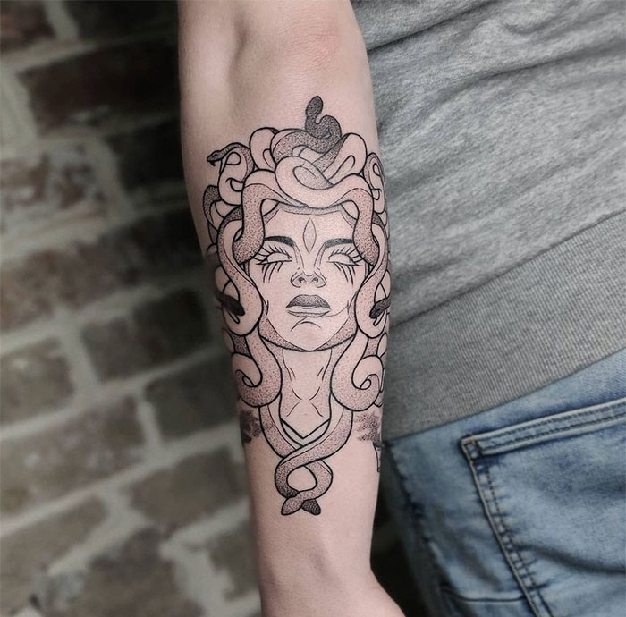 Medusa tattoo on forearm with closed eyes, snakes in hair; bold black lines, intricate details signify beauty and power.