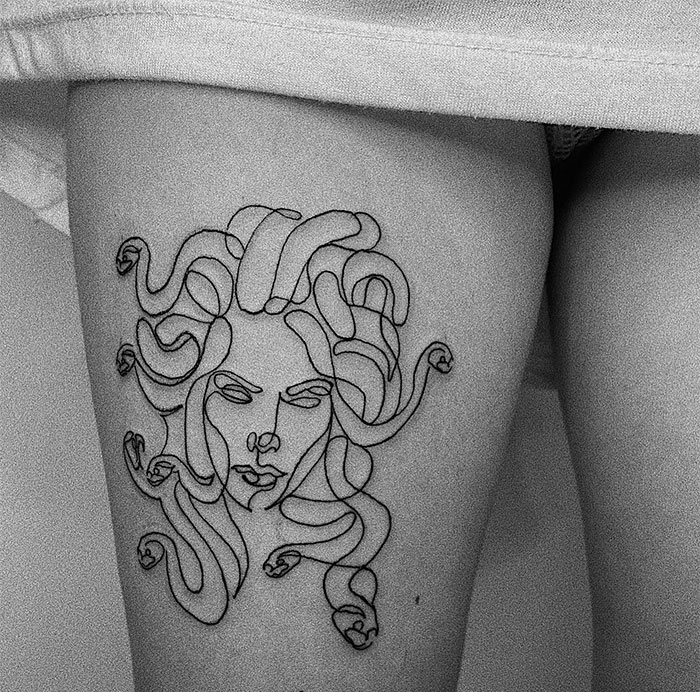 Minimalist Medusa tattoo on thigh, single-line style, abstract design showcasing beauty and defiance.