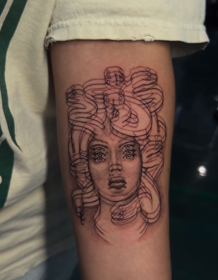 Surreal Medusa tattoo with multiple eyes and lips, surrounded by snakes; a symbol of beauty, power, and defiance.