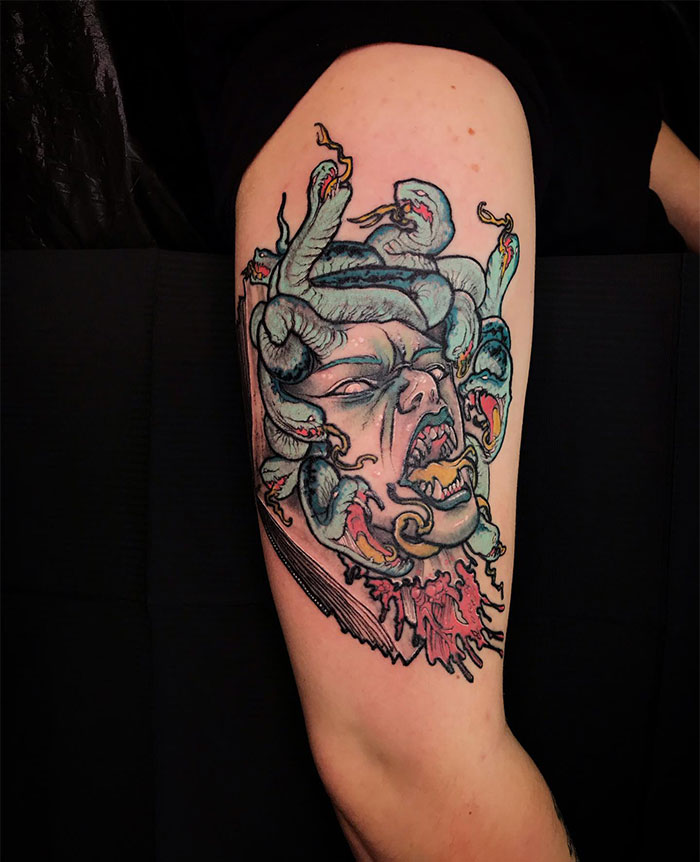 Colorful Medusa tattoo on upper arm with snakes, fierce face, vibrant details, and blood. Symbolizes beauty, power, and defiance.