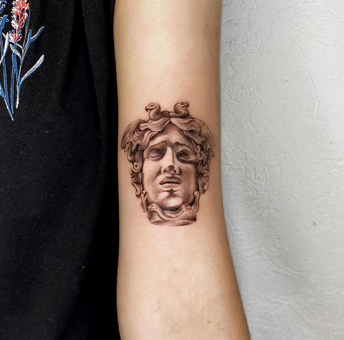 Realistic Medusa tattoo on forearm, showcasing detailed stone-like bust with classical sculpture style and intricate shading.