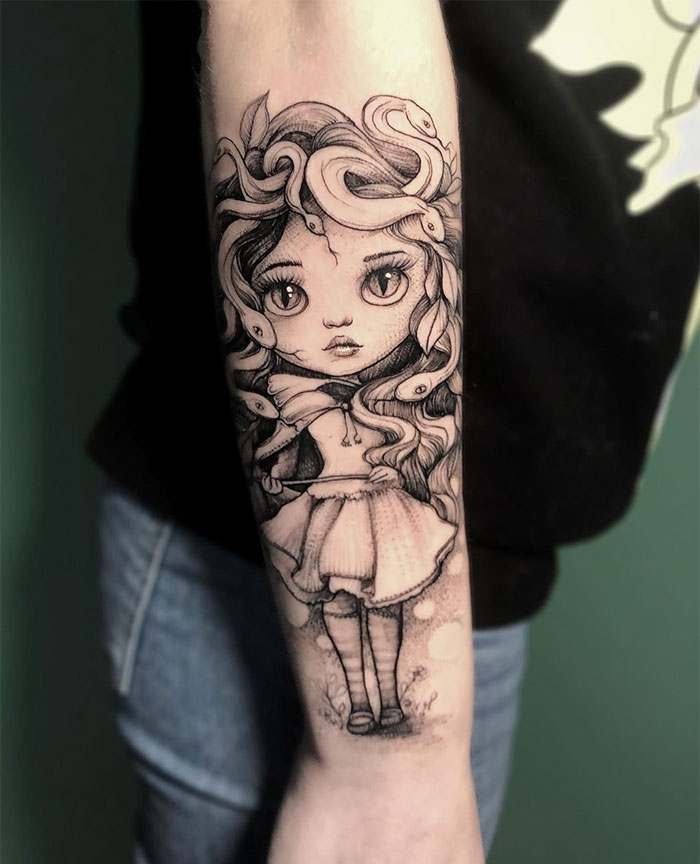 Whimsical Medusa tattoo on forearm; doll-like girl with snakes in curly hair, cartoon style, symbolizing beauty and power.