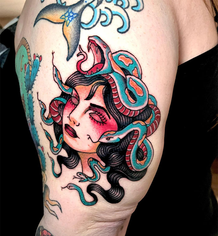 Medusa tattoo featuring a woman's face with closed eyes, black hair, and colorful snakes in red and blue hues.
