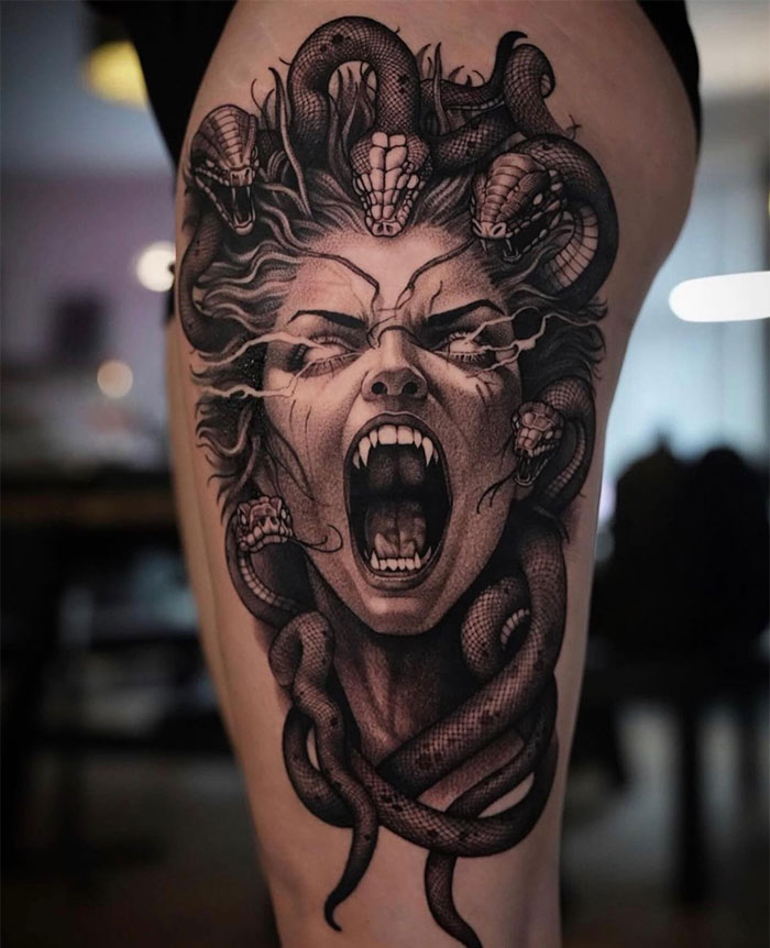 Fierce black and grey Medusa tattoo depicting a screaming woman with fangs and snake hair, symbolizing beauty and power.
