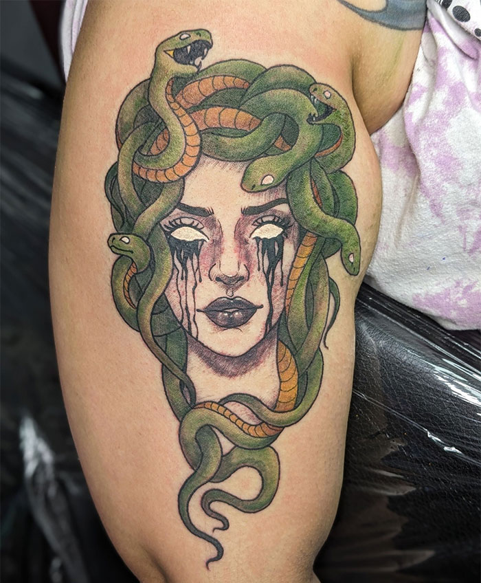 Vibrant Medusa tattoo with white eyes, black tears, and green snakes in hair, symbolizing beauty, power, and defiance.
