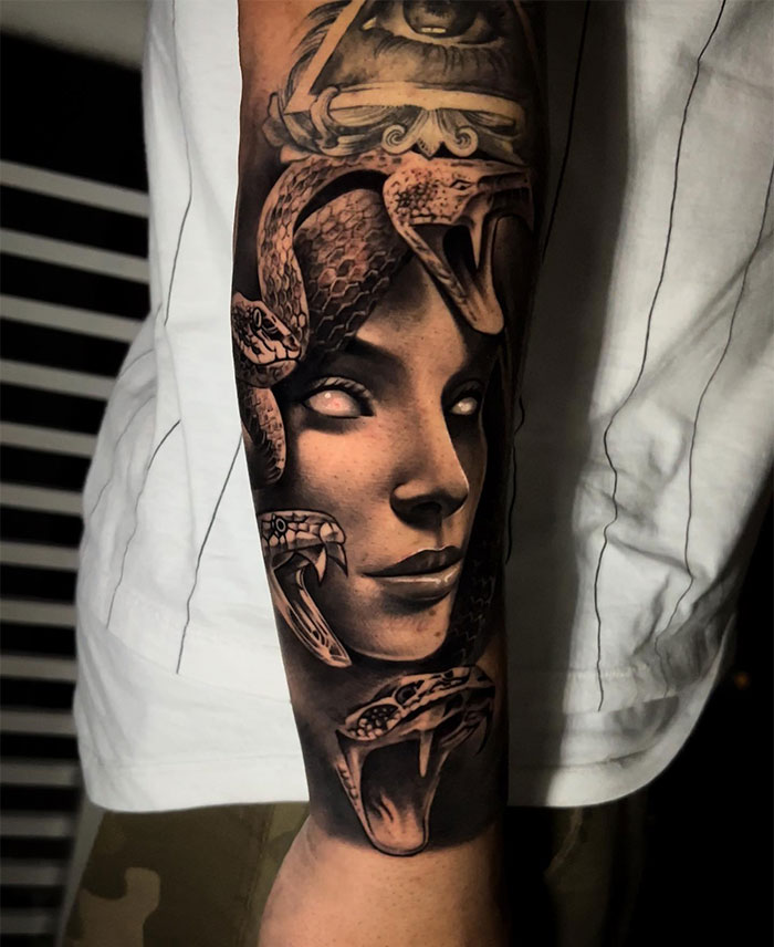 Realistic black and grey Medusa tattoo with a woman's face, glowing eyes, and detailed snakes.