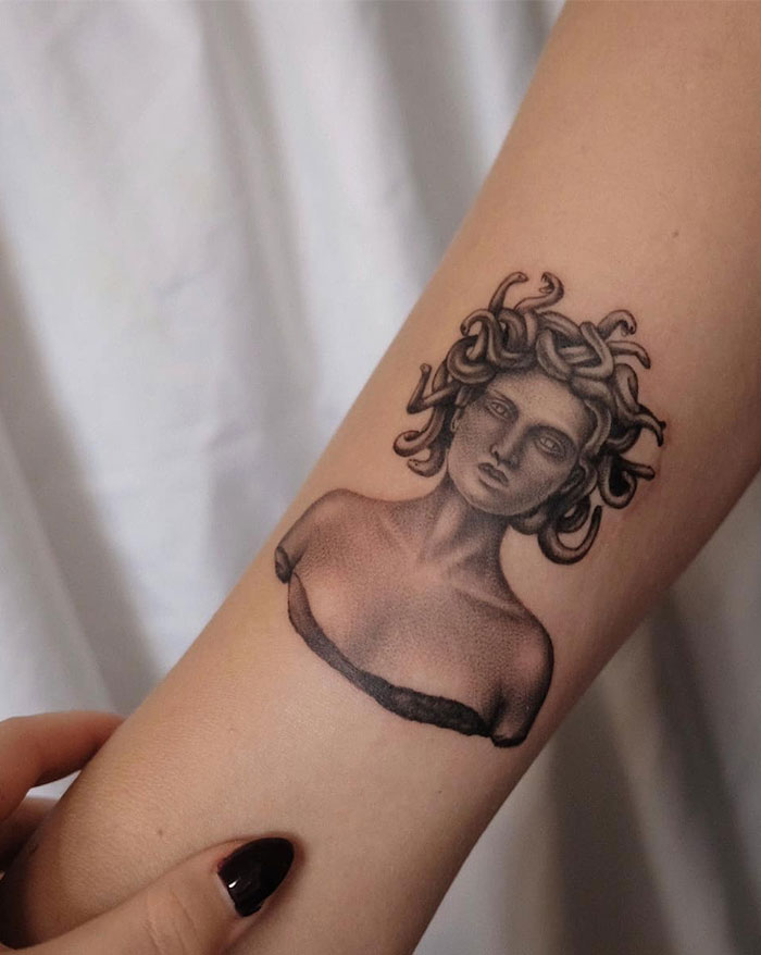 Realistic Medusa tattoo on forearm, showcasing classical sculpture style with intricate shading and snakes in her hair.