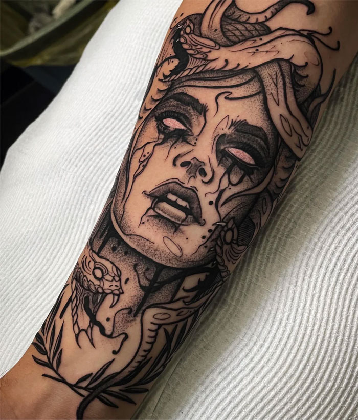 Dark Medusa tattoo on forearm, featuring a woman's face with snake hair, intense shading, and tears.