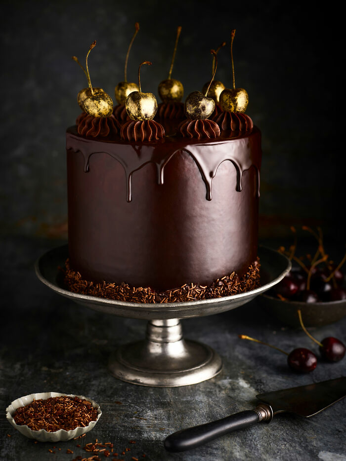 Elegant chocolate cake with gold-dusted cherries on top, styled to celebrate National Cake Day by photographers worldwide.