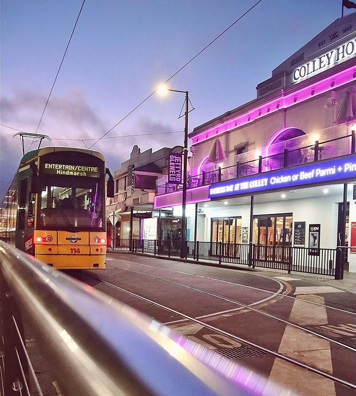 Tram passing by a vibrant bar with purple lights in Hindmarsh.