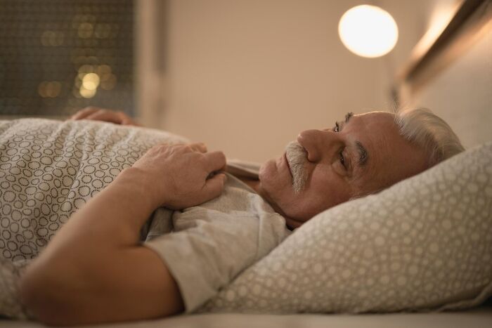 Elderly man lying awake in bed at night, reflecting on mind-blowing coincidences that seem impossible to be real.