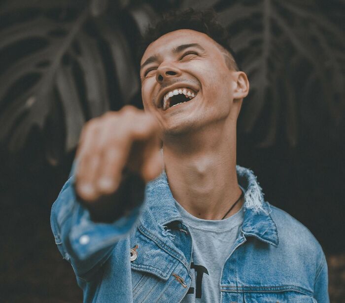Young man laughing and pointing, wearing a denim jacket, symbolizing awareness of toxic relationship red flags.