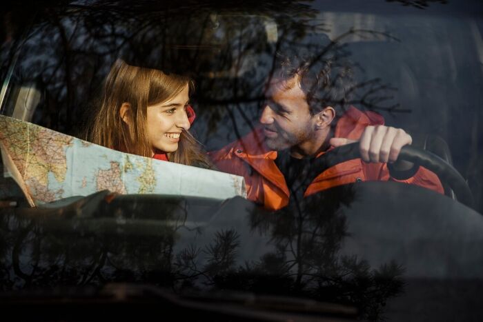Couple inside a car smiling and looking at a map, illustrating mind-blowing coincidences on a road trip adventure.