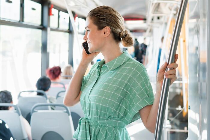 Young woman in a green dress holding a pole and talking on the phone inside a bus, illustrating mind-blowing coincidences.