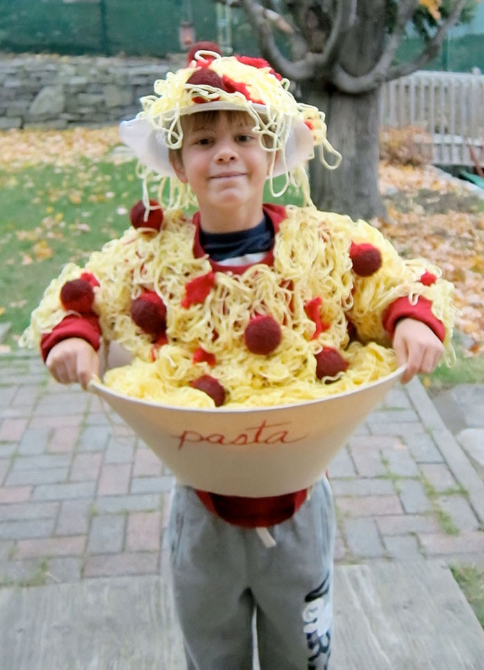 Child dressed in a creative kids Halloween costume holding a pasta bowl with yarn noodles and meatball details outdoors.