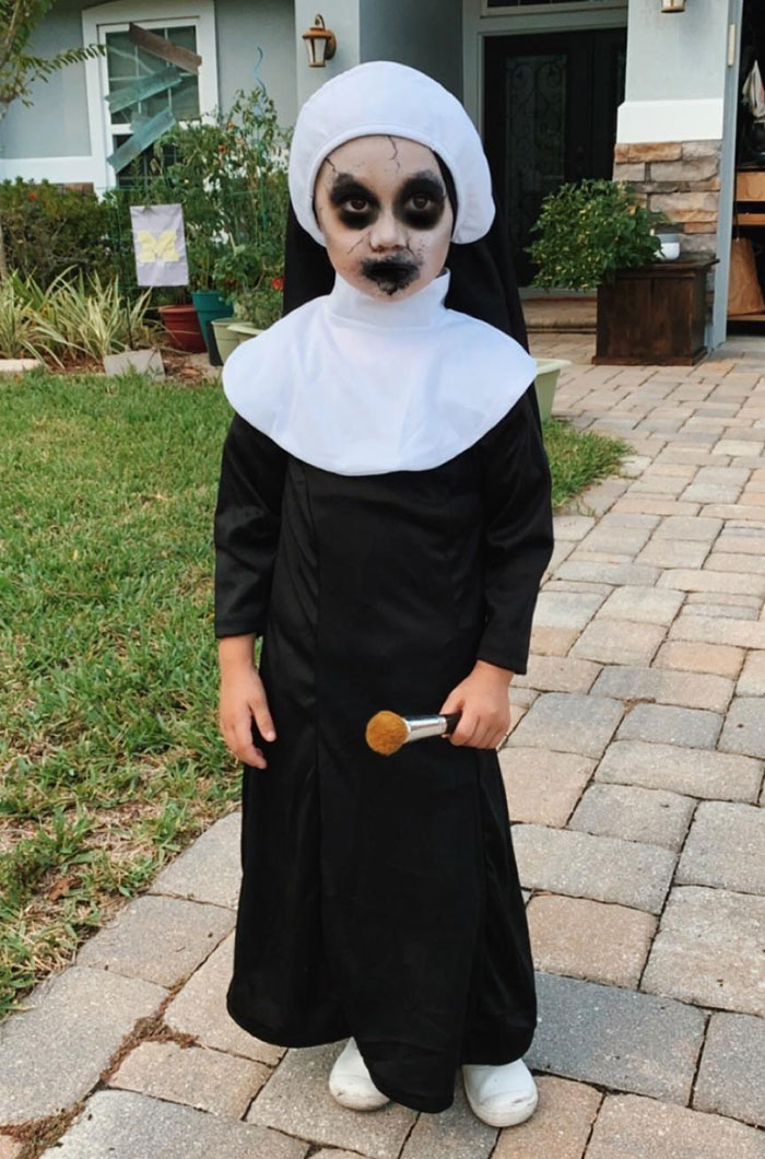 Child in scary Halloween costume makeup dressed as a spooky nun standing outdoors on a stone path for kids' Halloween costume ideas.