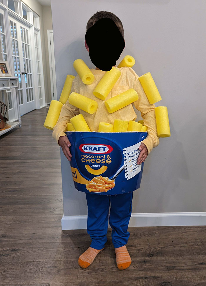 Child dressed in a creative kids Halloween costume wearing a macaroni and cheese box with foam noodles.